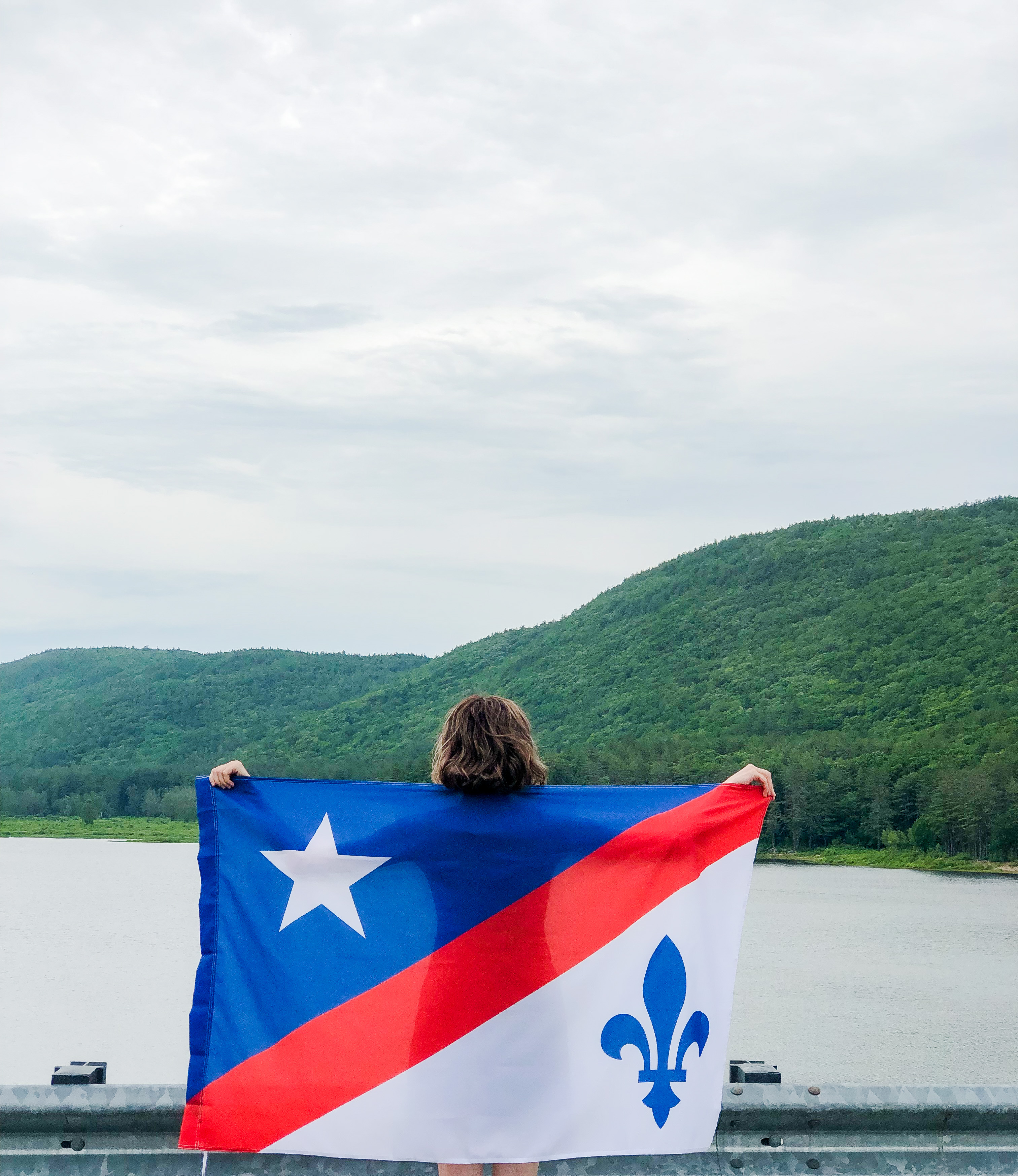 Young woman from the back holding the redesigned Franco-American flag with mountains in the distance.