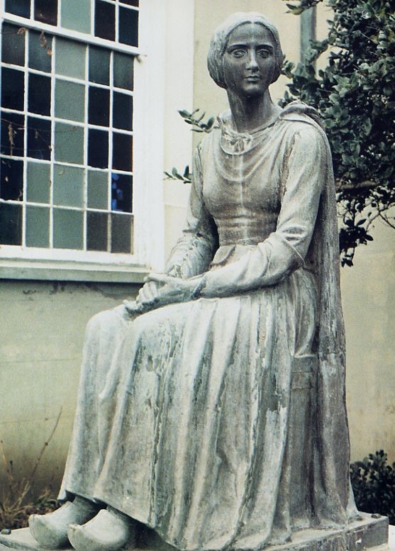 Statue of a young woman resembling Evangeline sitting with her hands in her lap and wearing a long dress with clogs.